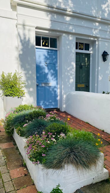 A charming small front garden in front of a white-painted house with a blue and a green door, each featuring the house number 78 above the door frames. The garden bed is edged with white concrete bord